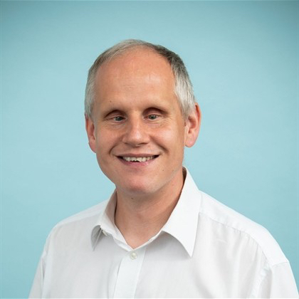 Dave smiling in front of a formal background.